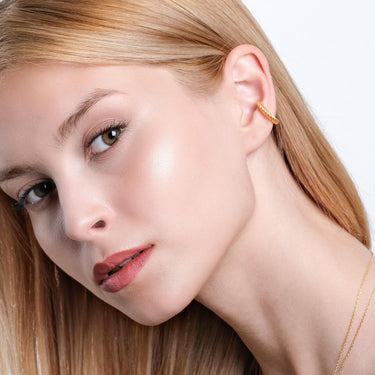 Close-up of a woman wearing a twisted gold vermeil ear cuff. She gazes off to the side, with her blonde hair neatly parted and draped over her shoulder.