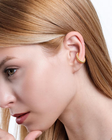 Profile view of a woman wearing an 18K gold vermeil twist ear cuff on her ear.