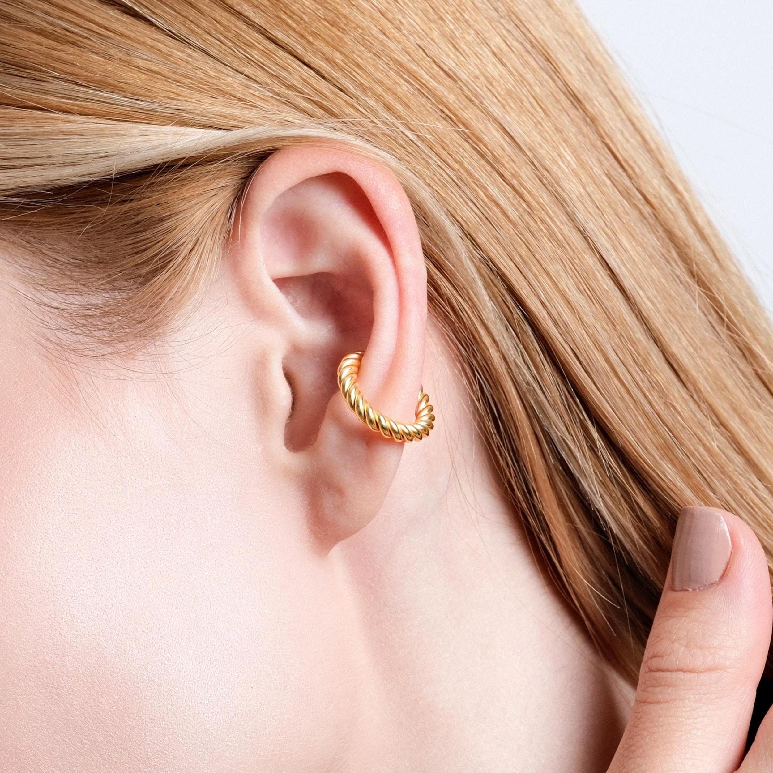 Close-up of a woman's ear showcasing a gold vermeil twisted ear cuff wrapped around the upper cartilage, with the woman gently holding her ear.