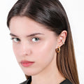 A close-up portrait of a woman with light skin and dark brown hair, wearing an 18K gold vermeil chunky hoop earring along with a thin, sparkling ear cuff.