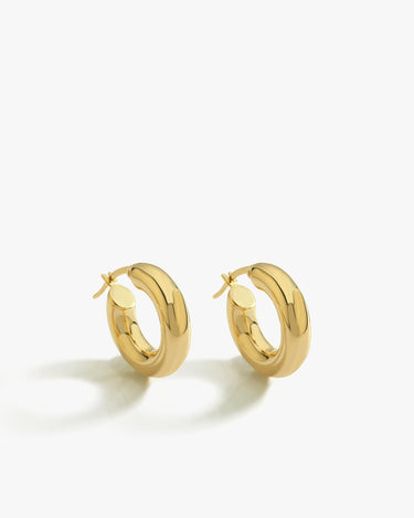 A pair of shiny 18K gold vermeil chunky hoop earrings laid side by side on a clean white surface, showcasing their thick, rounded design.