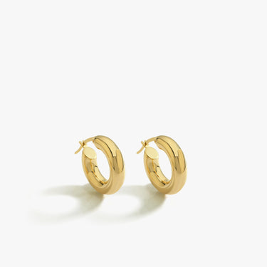 A pair of shiny 18K gold vermeil chunky hoop earrings laid side by side on a clean white surface, showcasing their thick, rounded design.