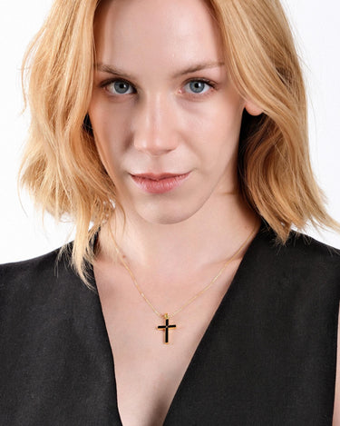 Woman looking directly at the camera while wearing a 14K gold vermeil black cross necklace, the pendant centered on her chest.