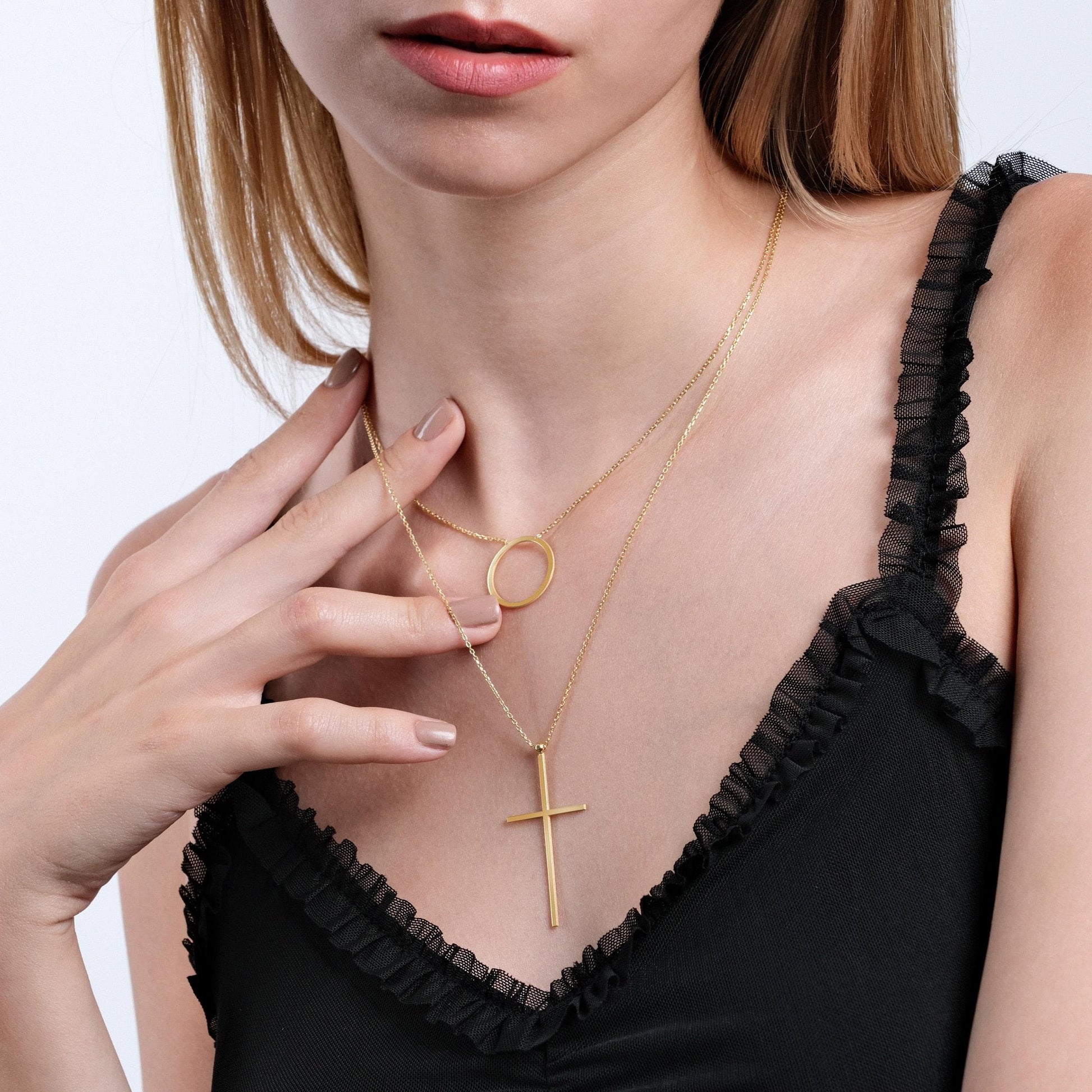 Close-up of a woman wearing an 18K gold vermeil layered necklace featuring a simple cross pendant and a round pendant, paired with a black ruffled camisole