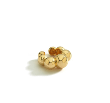 Isolated gold ear cuff with spherical beads on a white background.