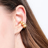 Close-up view of a gold ear cuff with spherical beads, worn on the upper part of a woman's ear.