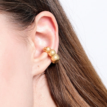 Close-up view of a gold ear cuff with spherical beads, worn on the upper part of a woman&#39;s ear.