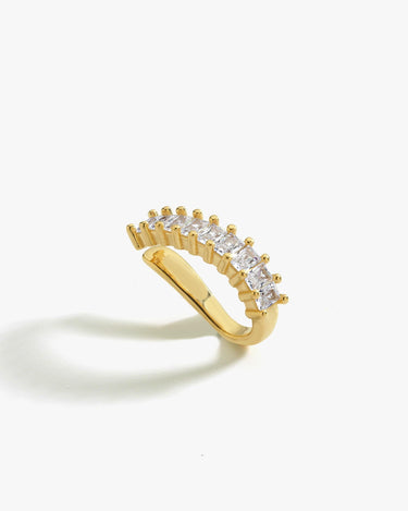 A gold ear cuff with baguette-cut clear stones, positioned on a white background. The cuff has a gently curved design, creating an elegant and minimalistic look.