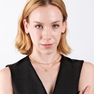 Portrait of a woman with fair skin and short blonde hair, wearing a black sleeveless top, paired with an 18K gold vermeil mushroom necklace layered with another gold chain.