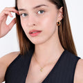 Close-up of a woman with light skin and straight brown hair, wearing a sleeveless dark top, showcasing an 18K gold vermeil mushroom necklace with a delicate chain.