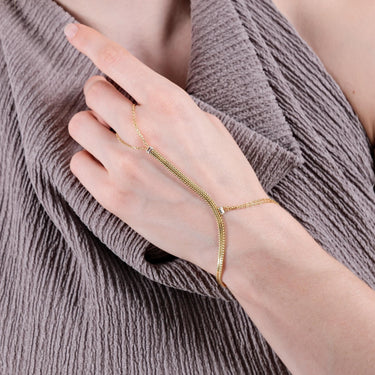 Close-up of a hand wearing a gold vermeil herringbone hand chain bracelet, with a textured taupe fabric in the background.