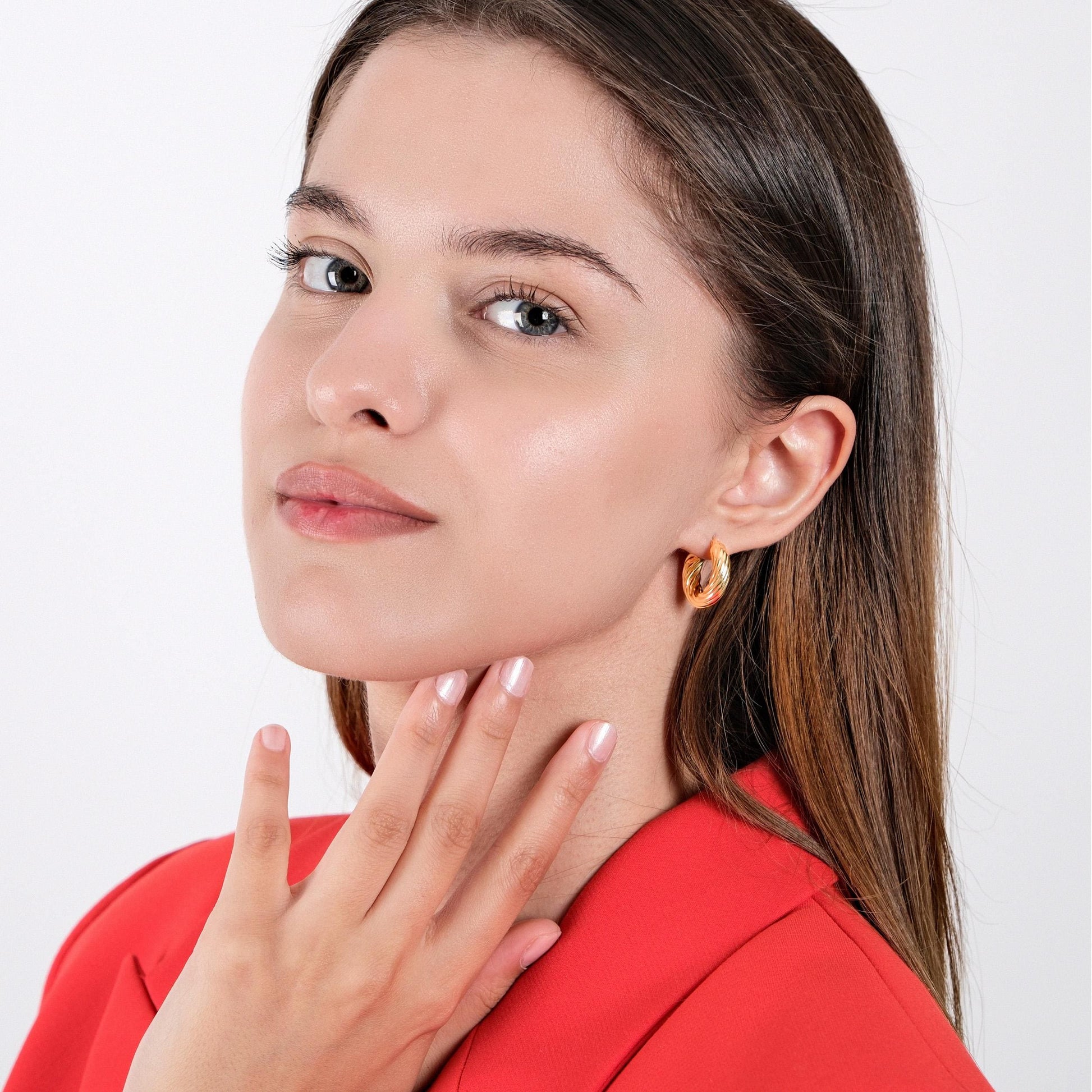 Woman wearing 18K gold vermeil chunky hoop earrings, gently touching her neck, while dressed in a red blazer.