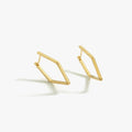 Geometric gold earrings from Mionza Fine Jewelry, lying on a flat surface, with the angular design casting subtle shadows, highlighting their modern, minimalist style.