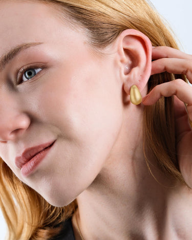 A woman with blonde hair touching her 18K gold vermeil tear drop earring.