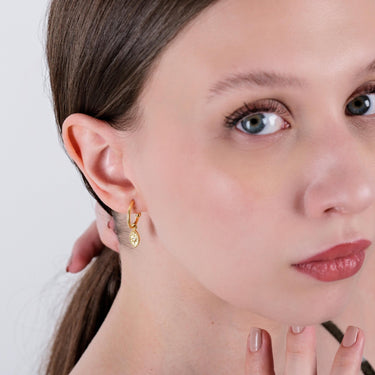 Partial view of a woman&#39;s face wearing a gold vermeil North Star and evil eye earring. The earring is an oval-shaped pendant hanging from a small hoop, and she is holding her hair away from her face.