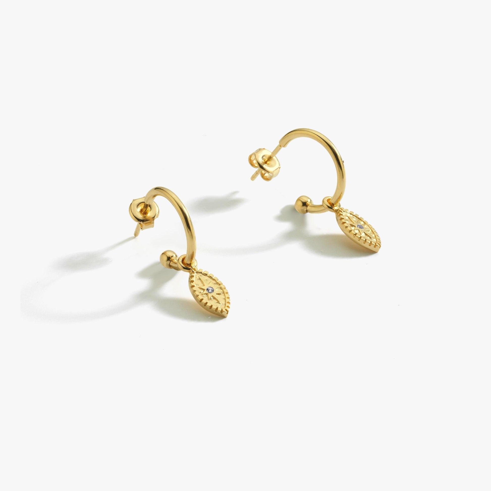 18K gold vermeil North Star and evil eye hoop earrings displayed on a white surface. The earrings feature small oval pendants with intricate star detailing, crafted in gold vermeil.