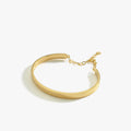 A side view of an 18K gold vermeil cuff bracelet with a chain extender, displayed flat on a white background.