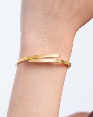 A close-up of a wrist wearing a minimalist 18K gold vermeil hinged bangle bracelet with a sleek, modern design.