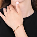 Close-up of a person’s hand gently touching their neck, wearing a thin, shiny gold vermeil bangle bracelet on their wrist. The person is dressed in a black top.