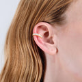 A side view of a woman&#39;s ear adorned with a gold ear cuff featuring clear stones. Her light brown hair is tucked behind the ear, showcasing the cuff&#39;s placement.