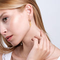 A woman gently touching her ear, showcasing the 18k gold vermeil snake dangle earrings.