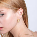 A profile shot of a woman with blonde hair and light skin wearing a thick 18K gold vermeil chunky hoop earring, paired with a small, delicate earring in the upper ear.