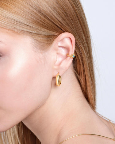 A profile shot of a woman with blonde hair and light skin wearing a thick 18K gold vermeil chunky hoop earring, paired with a small, delicate earring in the upper ear.