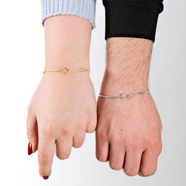 Two hands displayed vertically, one wearing a 14K gold vermeil bracelet and the other a matching silver bracelet, showcasing the elegant loop detail on both.