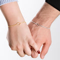 A close-up of two hands gently holding, highlighting a pair of matching bracelets: one in gold vermeil and the other in silver, both designed with a central knot feature.