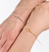 A close-up view of two hands side by side, one wearing a thin gold vermeil bracelet and the other a silver one, both featuring an elegant, minimalist loop design.