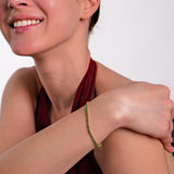 A model in a burgundy dress smiling softly, showcasing the elegance of an 18K gold vermeil emerald tennis bracelet.