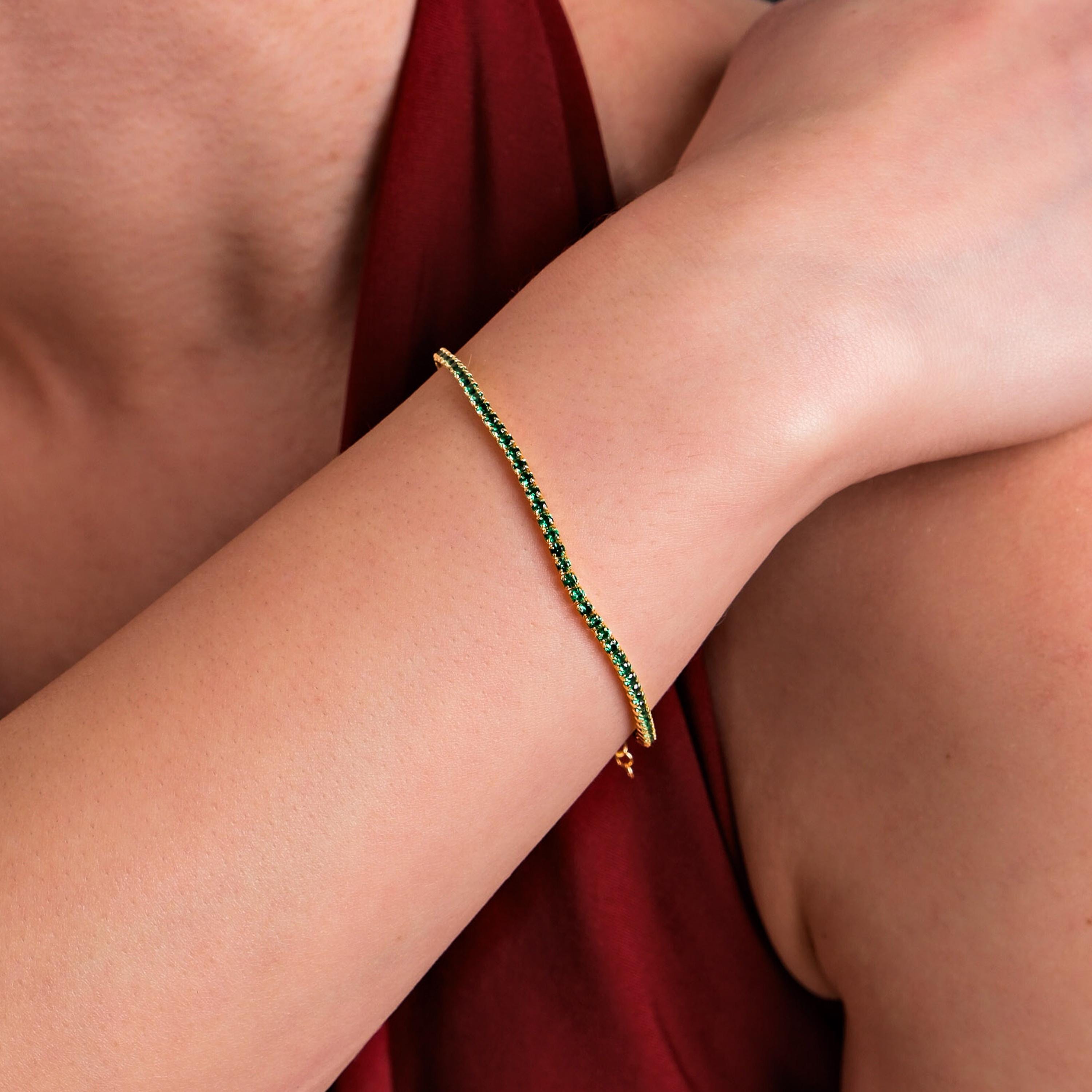 A close-up of a wrist adorned with an 18K gold vermeil emerald tennis bracelet, featuring a delicate row of vibrant green stones.