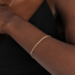 A close-up of a delicate 14K gold bracelet with a subtle shine, complementing the skin.