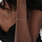 A sleek 14K solid gold chain bracelet elegantly wraps around the wrist, reflecting light beautifully.