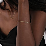 A sleek 14K solid gold chain bracelet elegantly wraps around the wrist, reflecting light beautifully.