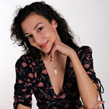 A woman wearing a floral dress, smiling while wearing the personalized gold necklace, emphasizing its elegant and sentimental design.