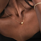 Side angle of a gold cube initial necklace resting on the wearer's collarbone.