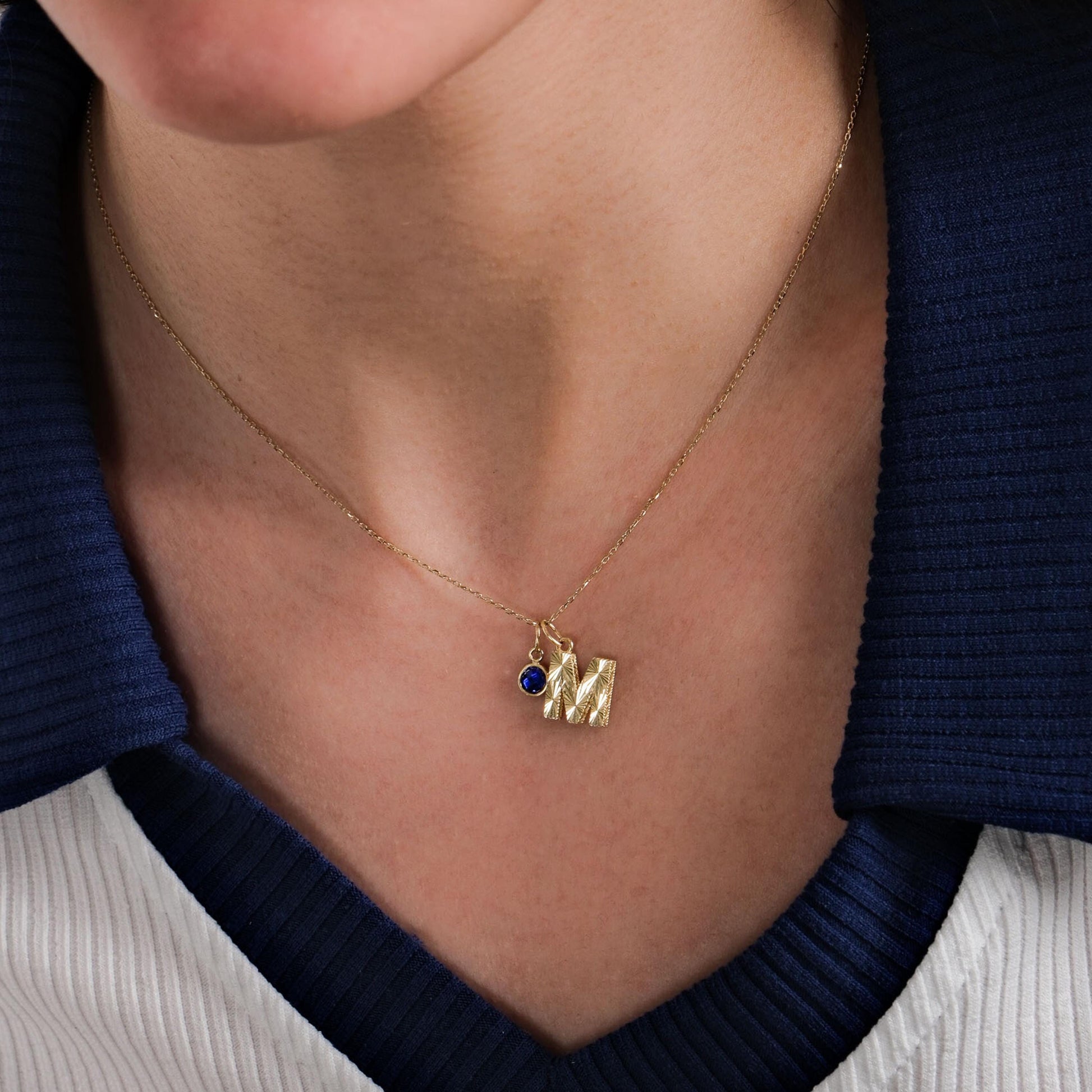 A close-up of a woman’s neckline adorned with a 14K Solid Gold Initial Necklace with Birthstone, perfectly complementing her navy and white outfit.