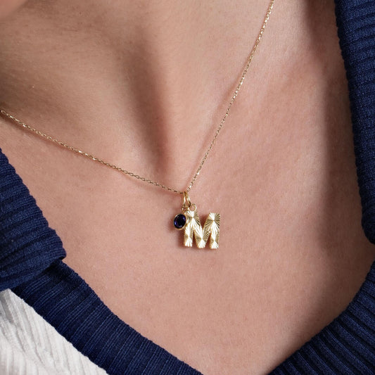 A delicate 14K Solid Gold Initial Necklace with Birthstone, featuring a textured gold letter charm and a deep blue birthstone, elegantly displayed on a woman&#39;s collarbone.