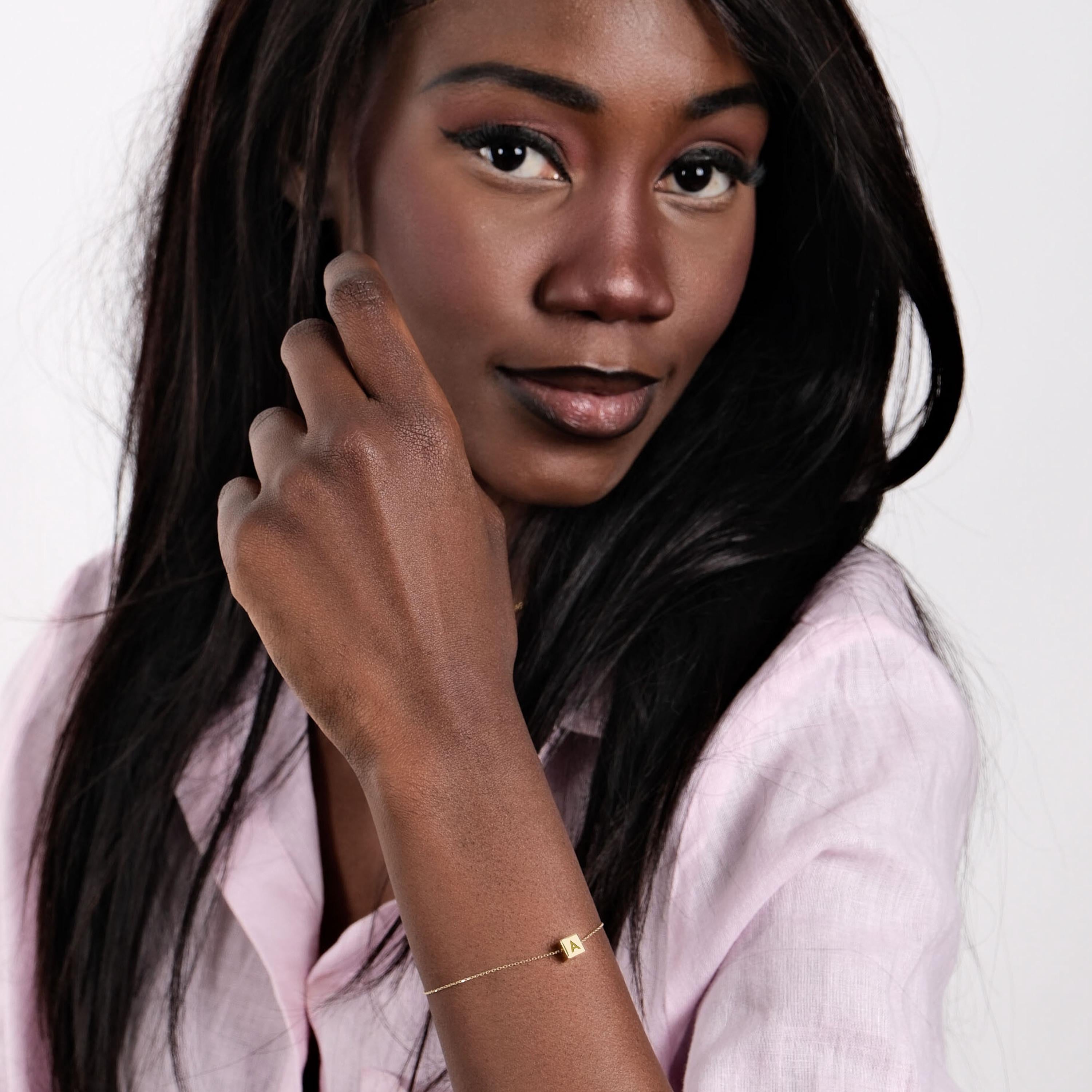 14K Solid Gold Cube Initial Bracelet – The model stylishly showcasing the personalized gold bracelet with a pink blouse.