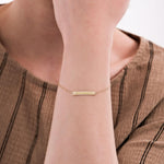 Close-up of a woman's wrist wearing a 14K solid gold engraved bar bracelet with Roman numerals on a delicate chain.