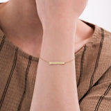 Close-up of a woman's wrist wearing a 14K solid gold engraved bar bracelet with Roman numerals on a delicate chain.
