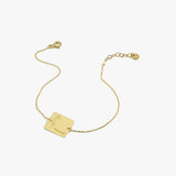 Minimalist 14K solid gold birthflower bracelet with a square plate engraved with a flower and the name “Rachel”.