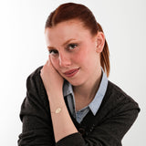 Red-haired woman looking down and smiling subtly while wearing a 14K solid gold custom bracelet engraved with “SHB”.