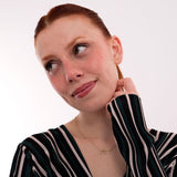 A playful shot of a woman gazing sideways with her hand on her face, wearing a striped top and a subtle 14K solid gold Arabic name necklace that glows against her skin.