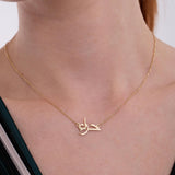 Close-up of a woman's neck wearing a delicate 14K solid gold Arabic name necklace with a fine chain, showcasing the intricate Arabic calligraphy in the pendant.