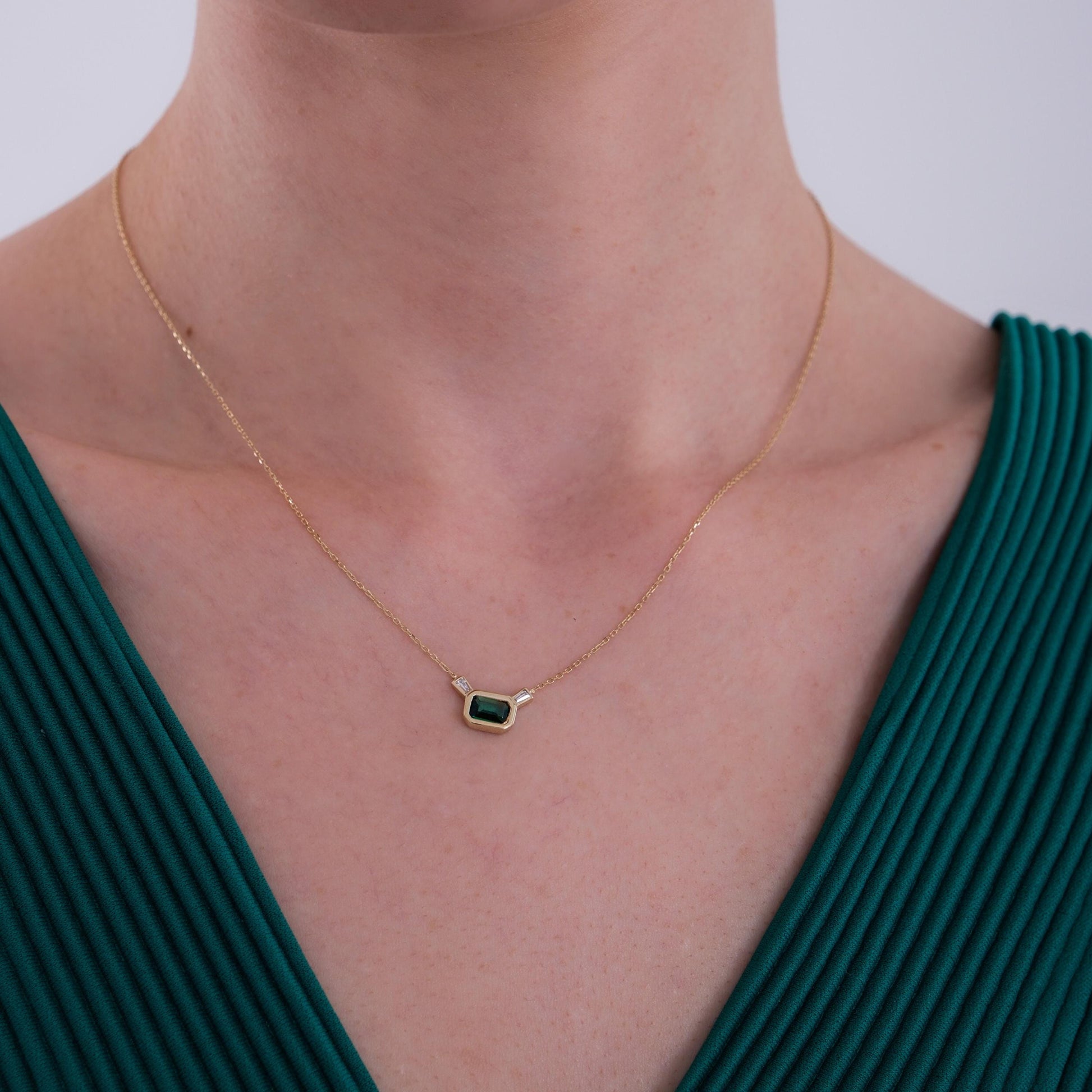 The 14K Solid Gold Emerald Cut Necklace is centered elegantly on the model’s chest, highlighting its delicate design against her green V-neck top.