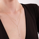 A delicate double-layered 14K solid gold pearl lariat necklace worn on a woman's neck, featuring a small pearl and a dangling 'K' initial charm.