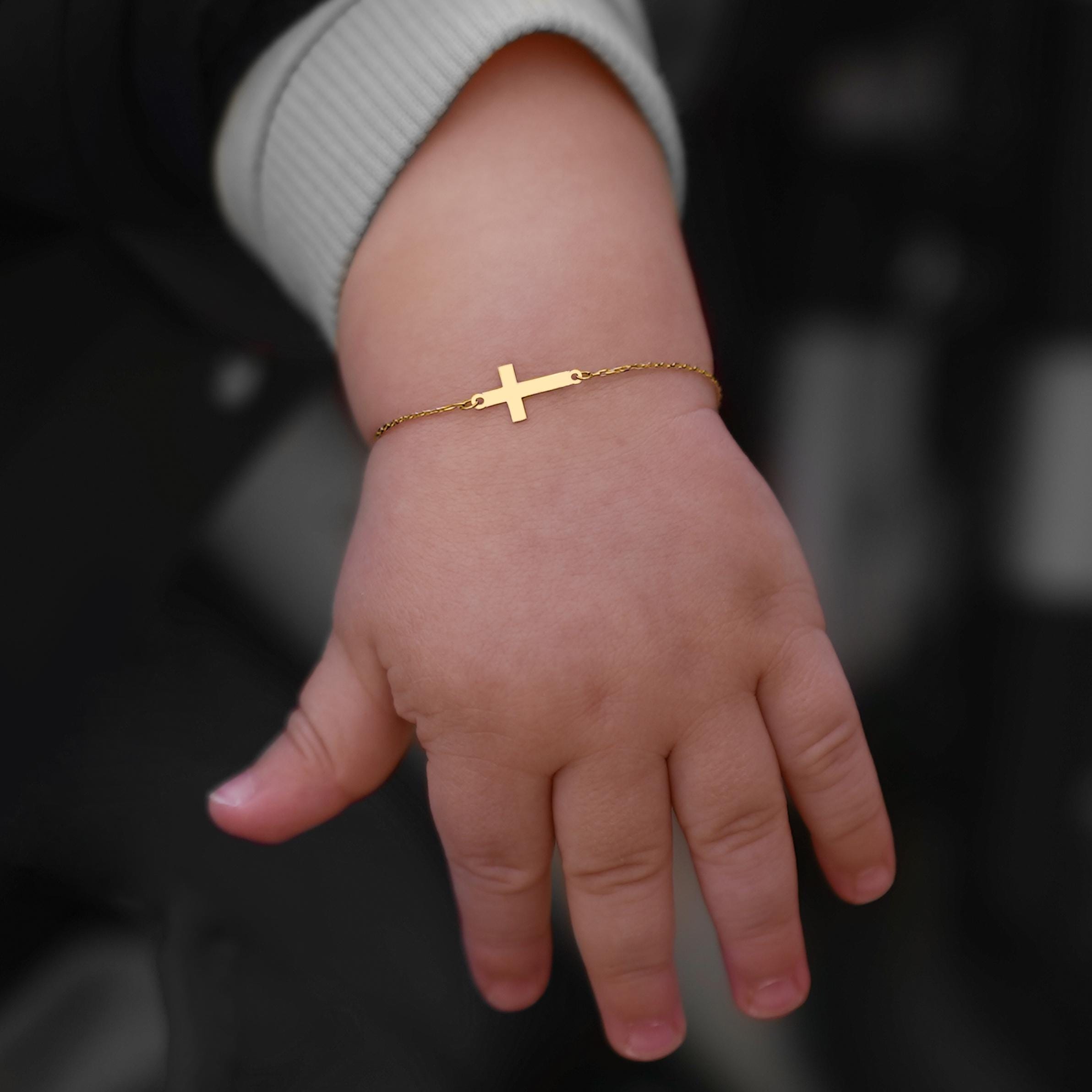 A child’s hand adorned with a First Holy Communion Bracelet, featuring a dainty gold cross.