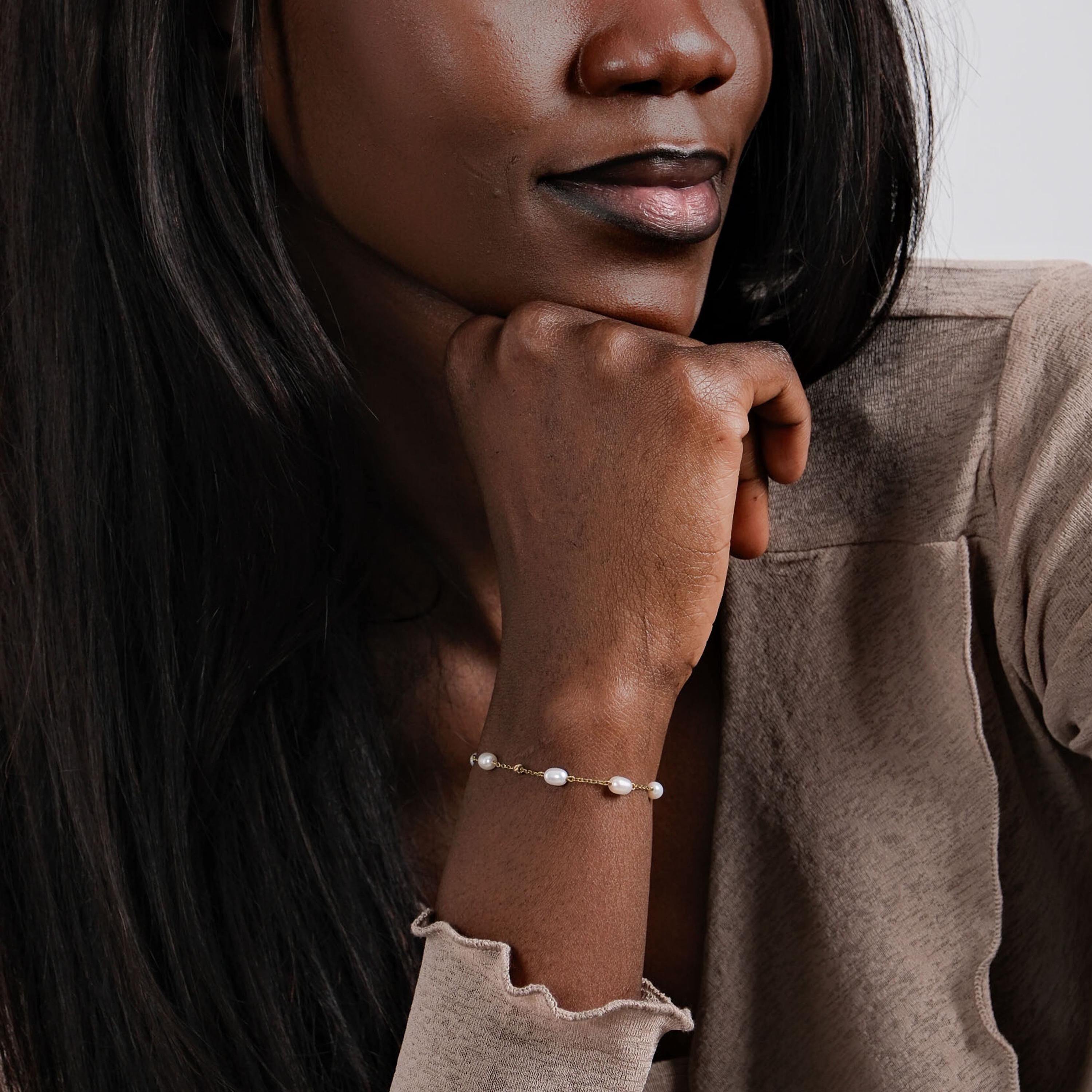 A stylish woman in a beige top gently resting her hand, emphasizing the timeless beauty of the 14K solid gold freshwater pearl bracelet.